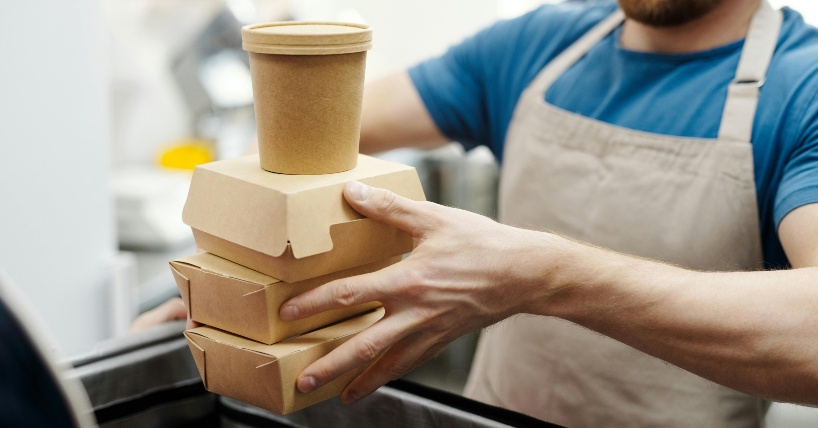 Čovek drži tri papirne kutije za hranu i papirnu čašu.