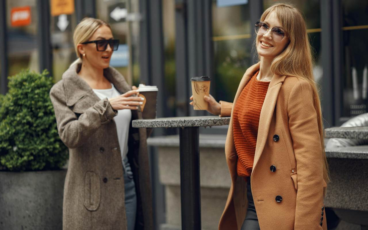 Dve žene u kaputu poziraju sa kafom u ruci.