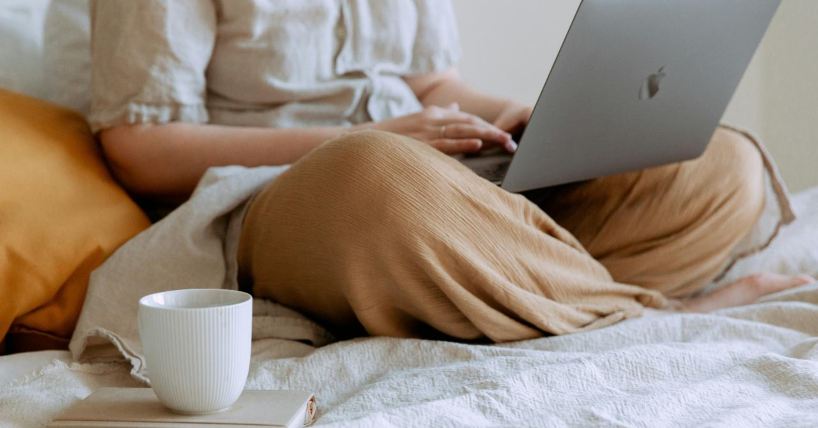 Žena sedi na krevetu i radi na laptopu