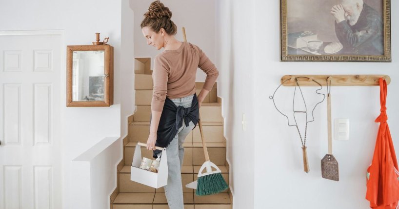 Žena koja drži u rukama metlu i sredstva za čišćenje se penje uz stepenice