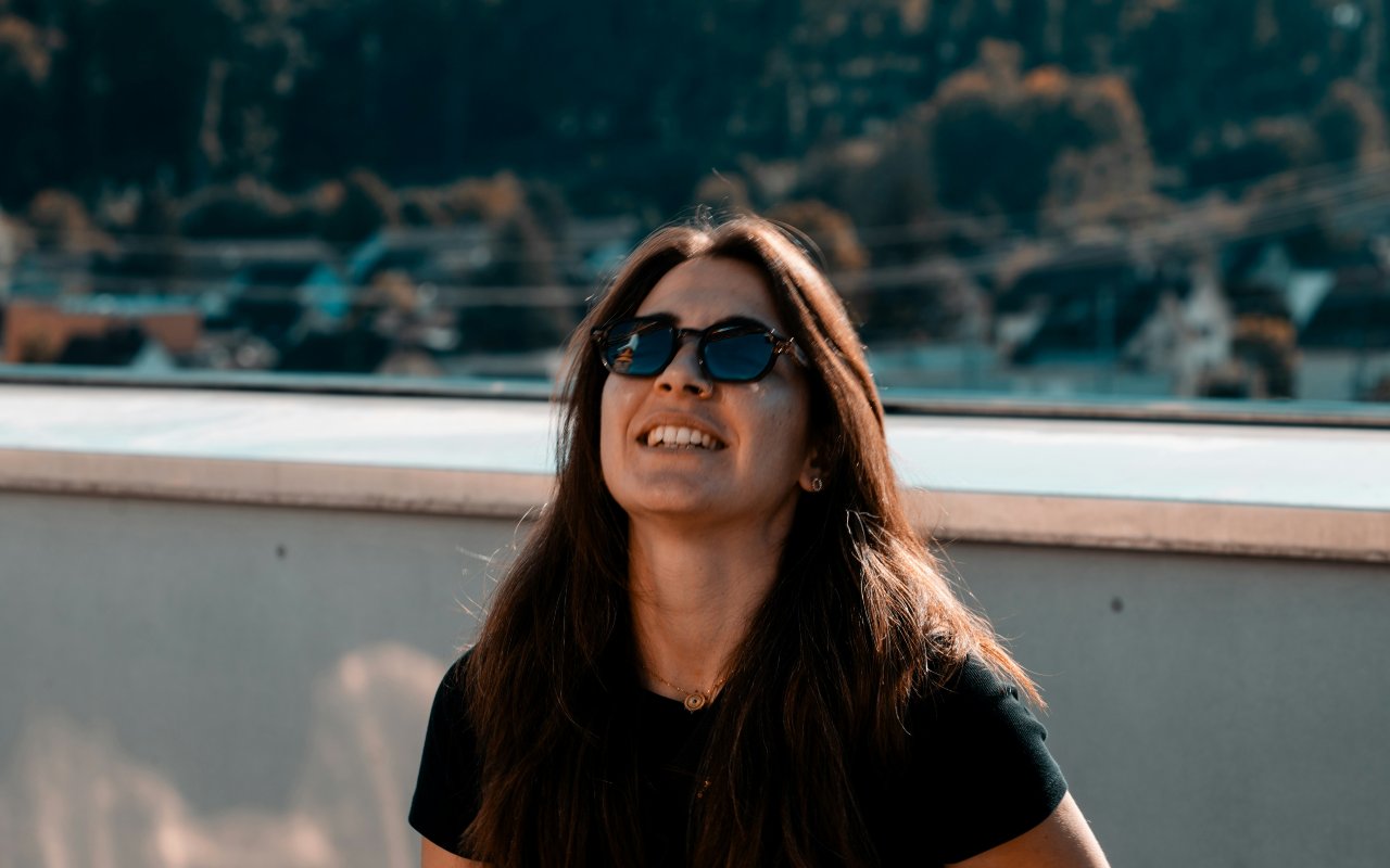 Mlada žena nasmejana napolju sa sunčanim naočarima.