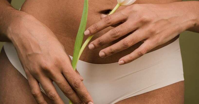 Žena u donjem vešu pozira sa cvetom u ruci